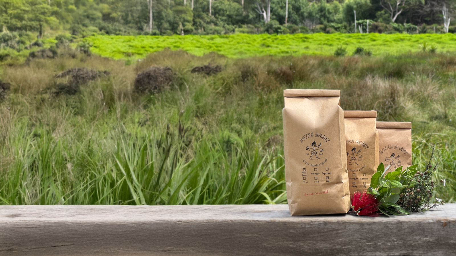 Three aotea roast coffee bags on a wooden surface with a natural landscape in the background
